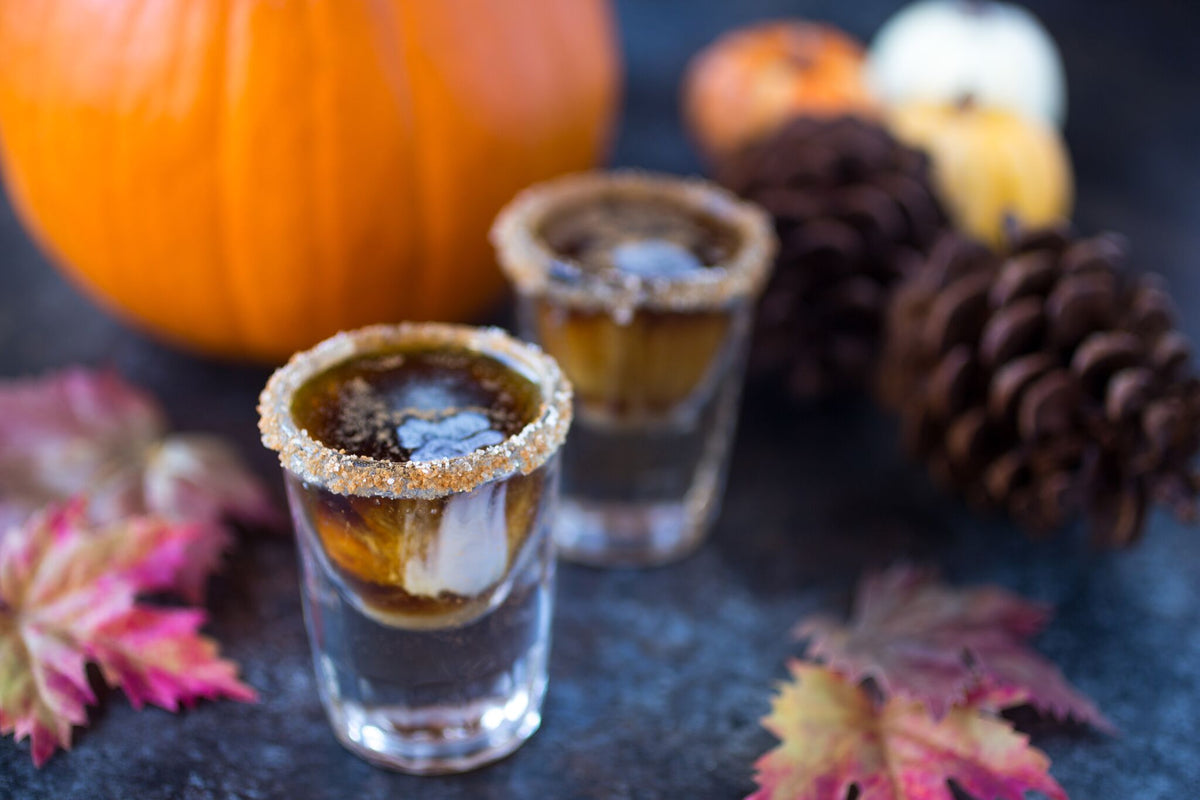 Two cinnamon sugar rimmed whiskey coffee shots with swirling cream, styled with a pumpkin, pinecones, and autumn leaves