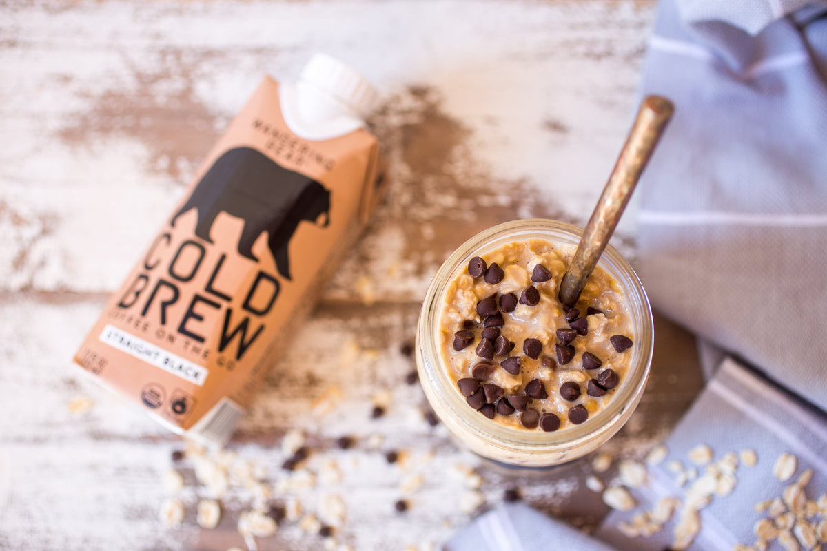 Jar of chocolate chip overnight oats with mini chocolate chips beside a cold brew carton on a wooden surface