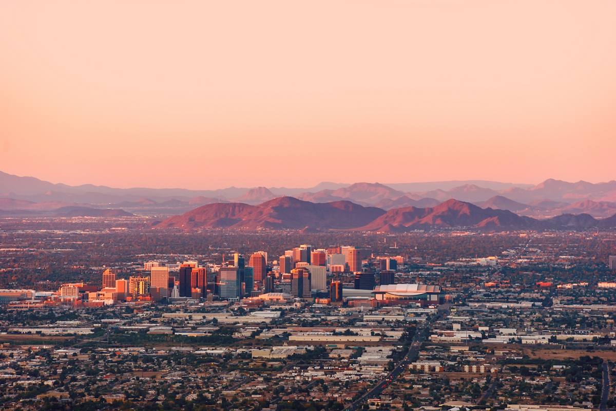 Downtown Phoenix skyline at sunset with foothills and a warm pink-orange sky
