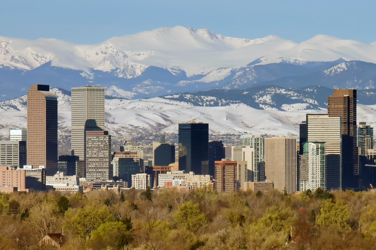 Denver skyline viewed from tree-lined foreground with snow-covered Rocky Mountains in the background