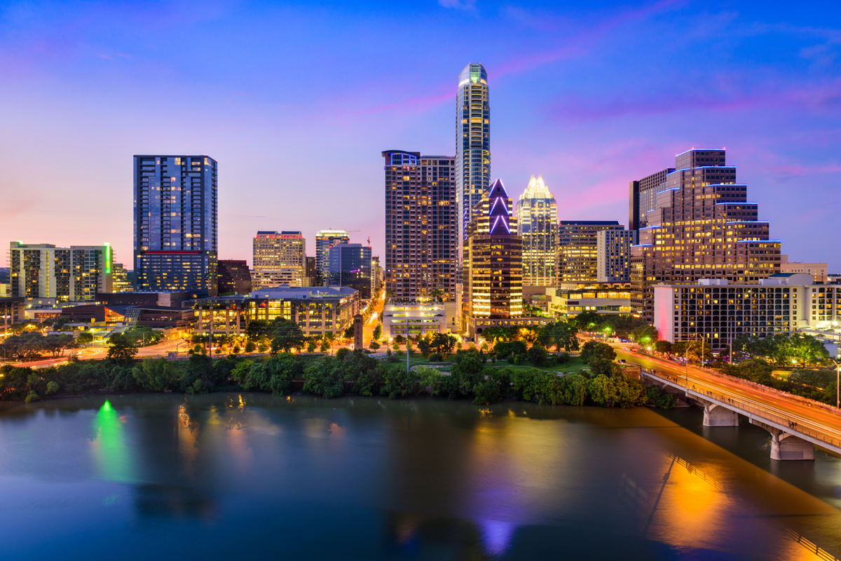 Austin skyline at dusk with illuminated downtown buildings and colorful reflections on the river