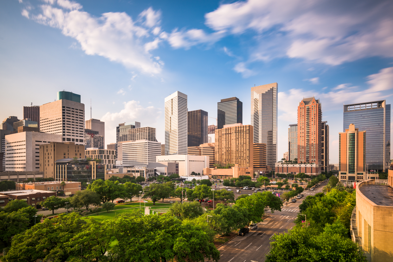 Downtown Houston skyline at golden hour with glass and brick skyscrapers rising above a tree-lined park