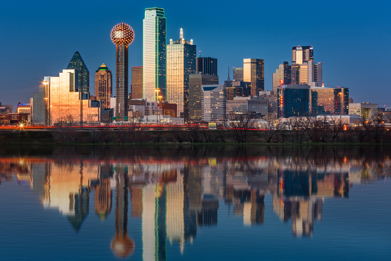 Dallas skyline at dusk reflected in a calm river, featuring Reunion Tower and downtown skyscrapers