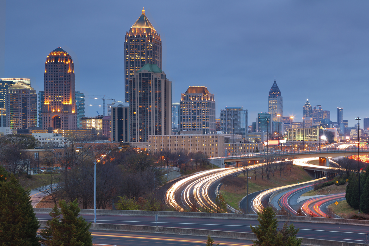 Atlanta skyline at dusk with illuminated skyscrapers and curving highway light trails in the foreground