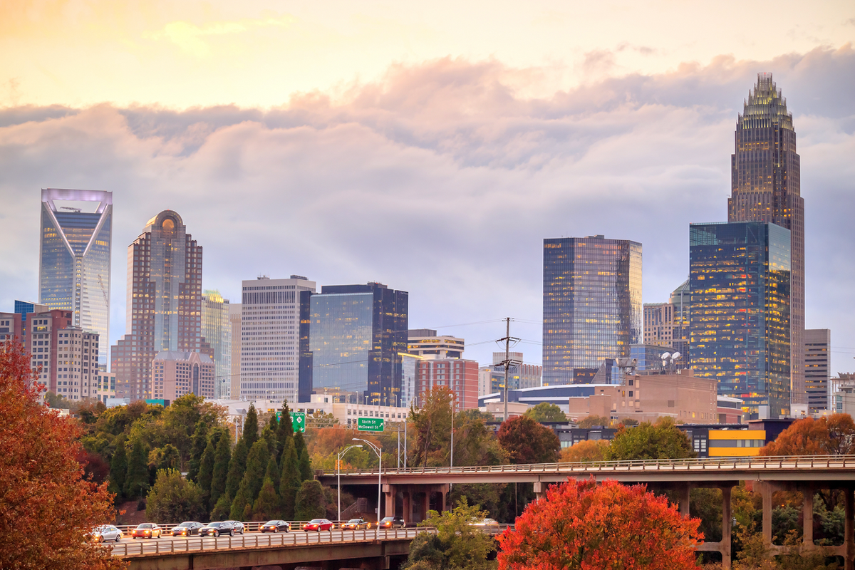 Charlotte skyline at sunset, Uptown skyscrapers with highway traffic and red autumn trees in foreground