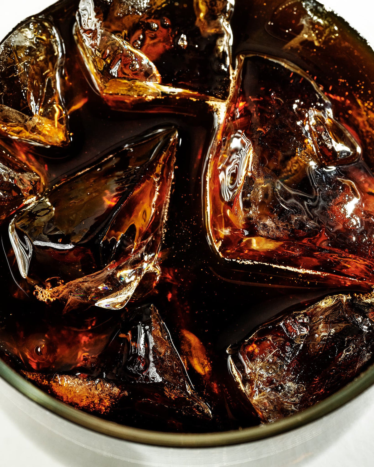 Close-up of a glass of cold brew coffee with large ice cubes showing dark amber color and glossy reflections against a white surface