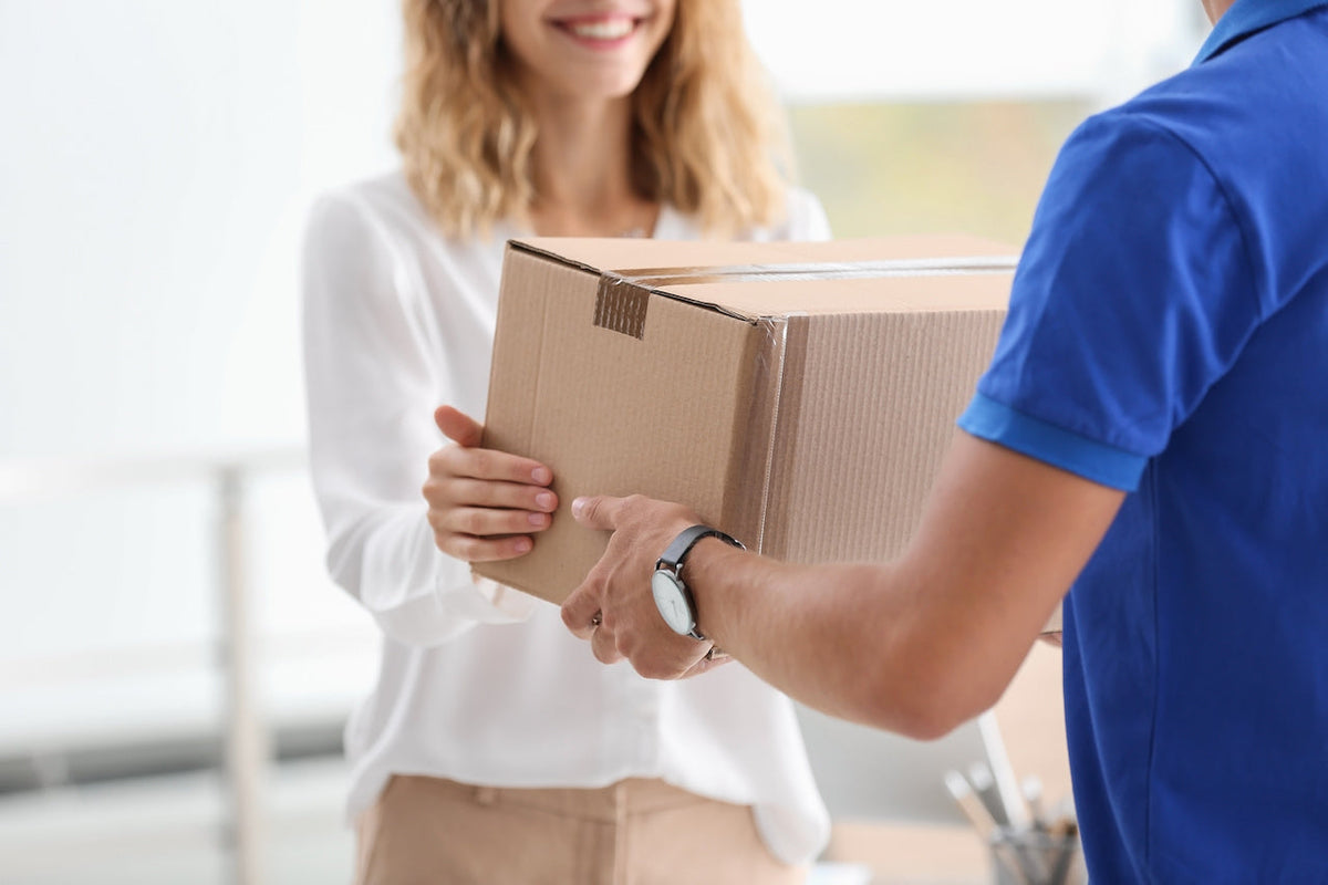 Delivery worker handing a cardboard box to a smiling woman in an office setting