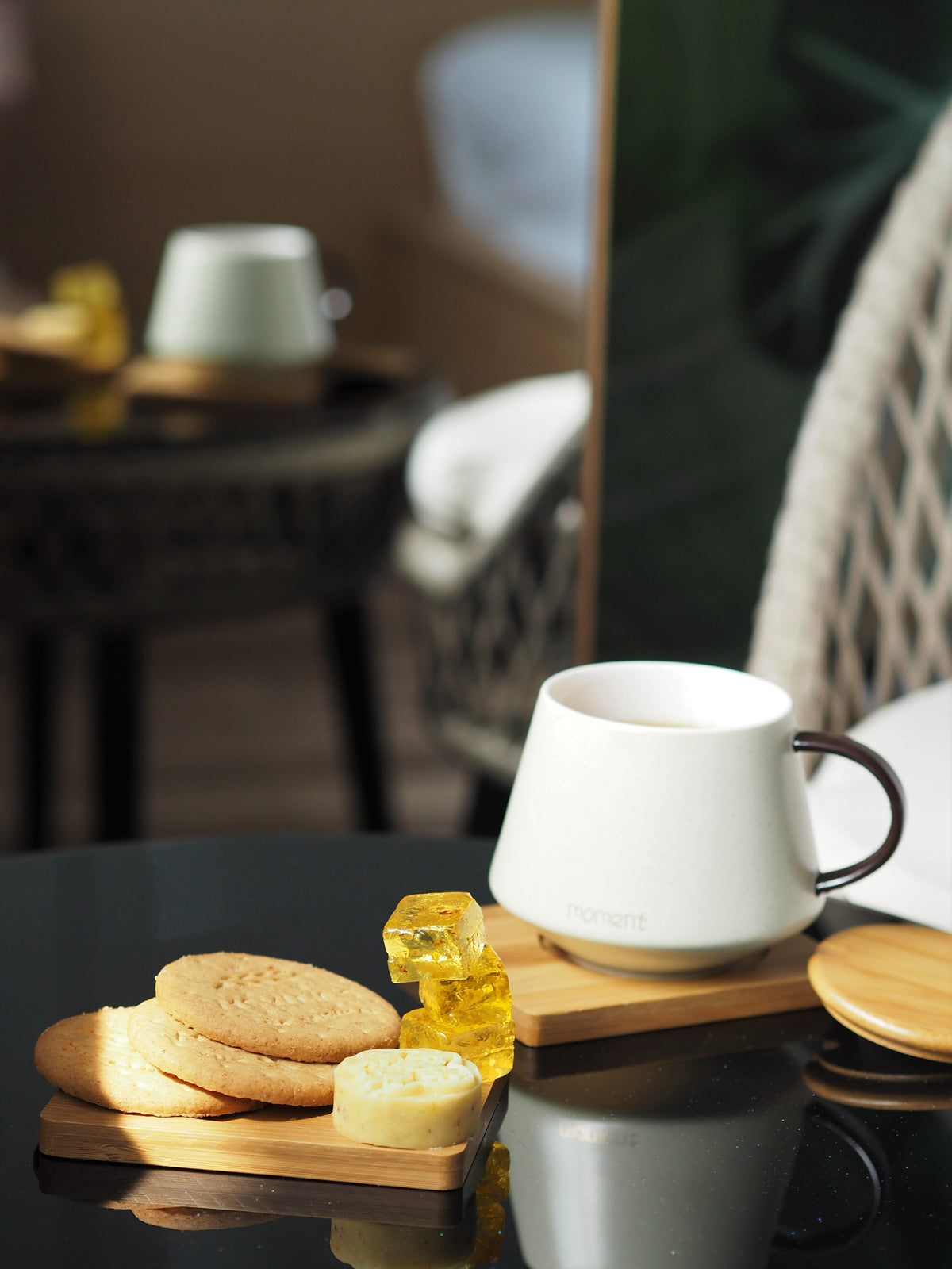 Close-up of a white ceramic coffee mug and stacked biscuits on a wooden board on a dark reflective table with a blurred background