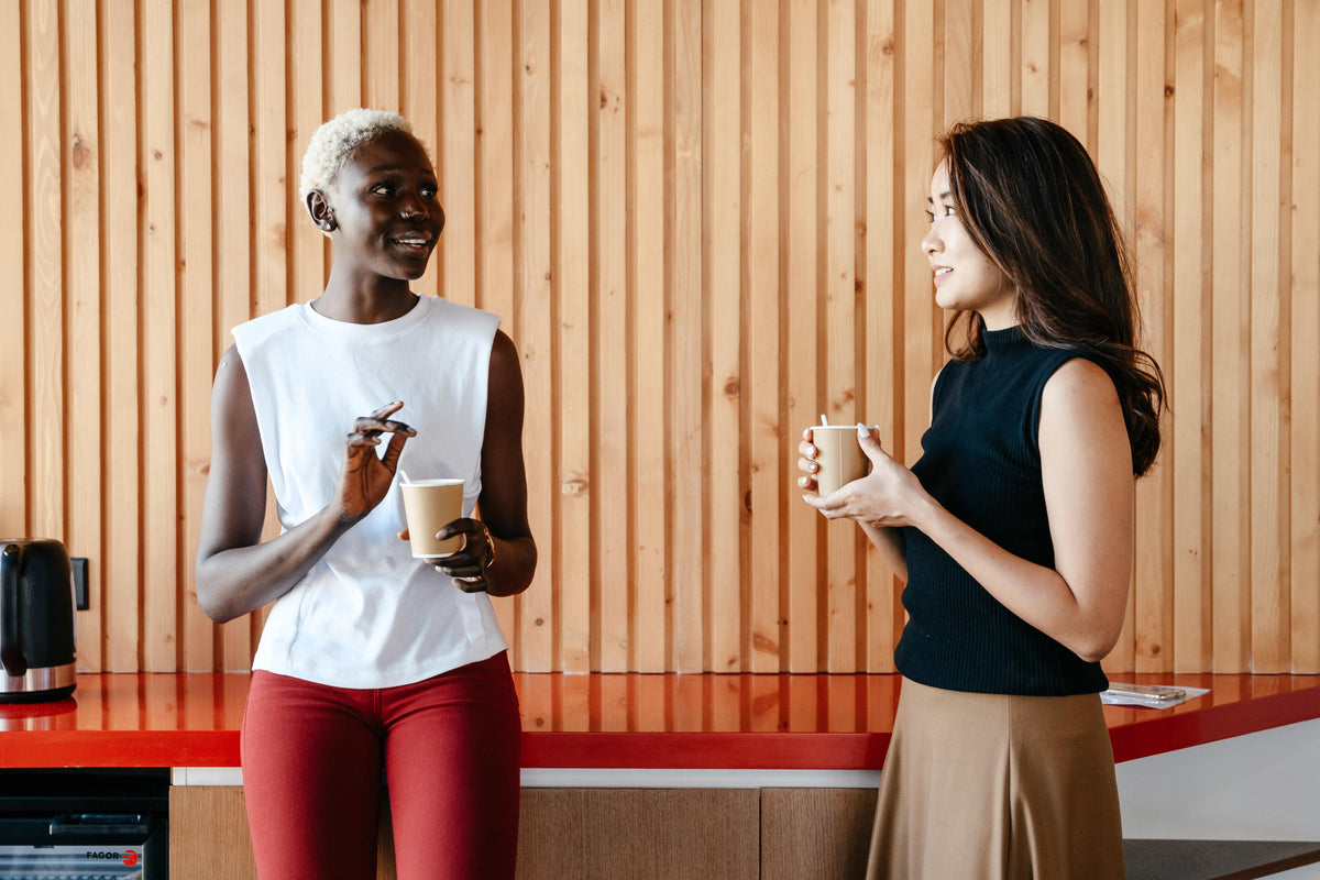 Two coworkers chatting over coffee in a break area with vertical wooden paneling