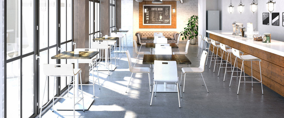 Sunlit office breakroom with white tables and chairs, wooden counter with coffee station and framed sign ‘COFFEE MENU’