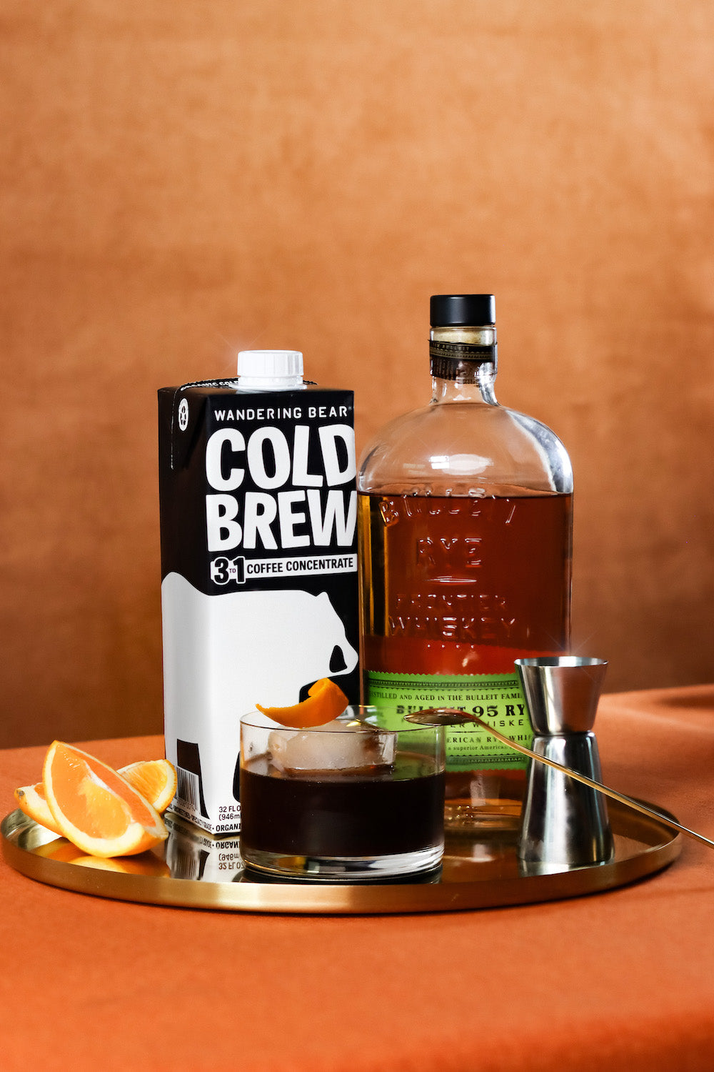 Wandering Bear cold brew concentrate 3:1 carton beside a rye and cold brew cocktail on a gold tray with orange garnish