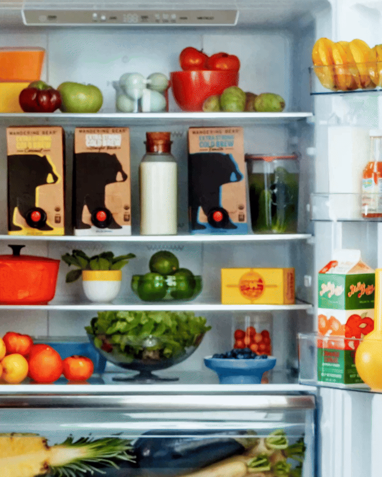 Wandering Bear boxed cold brew cartons in an open refrigerator with fruit, jars, and other groceries